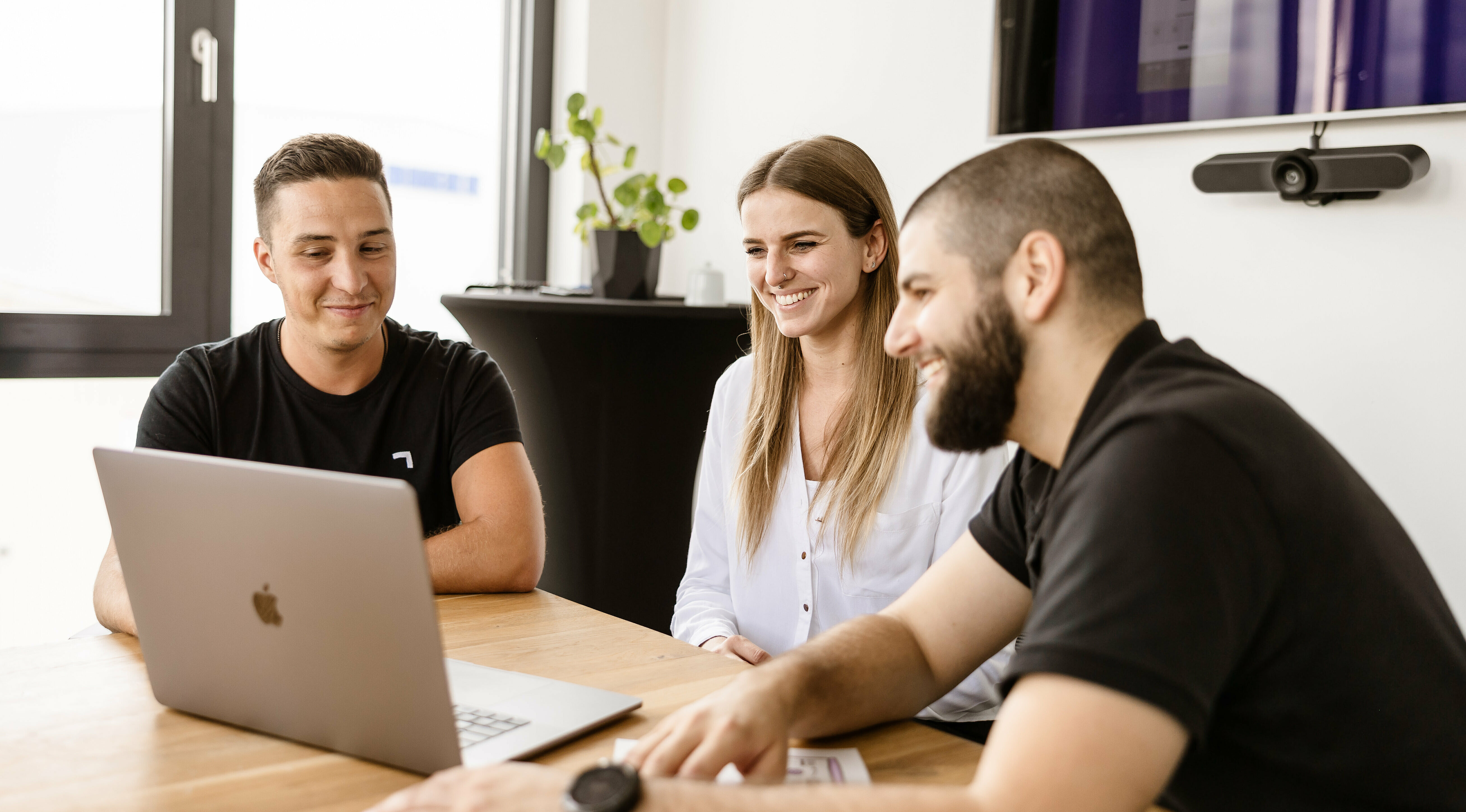 Drei LightsOn Mitarbeiter sitzen im Besprechungsraum und schauen lachend in einen Monitor