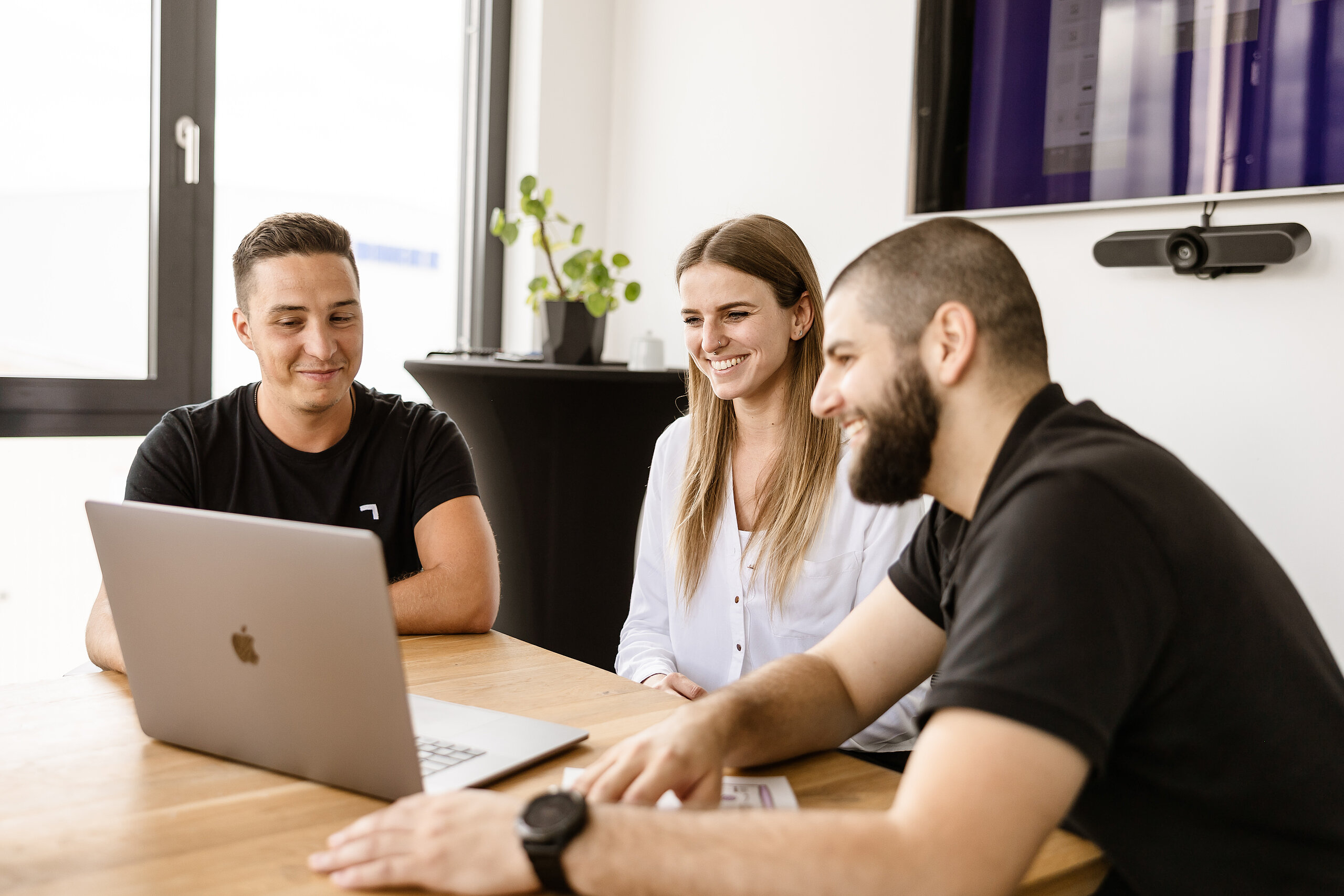Drei LightsOn Mitarbeiter sitzen im Besprechungsraum und schauen lachend in einen Monitor