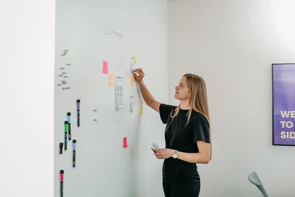Junge Frau klebt bunte PostIts an ein Whiteboard