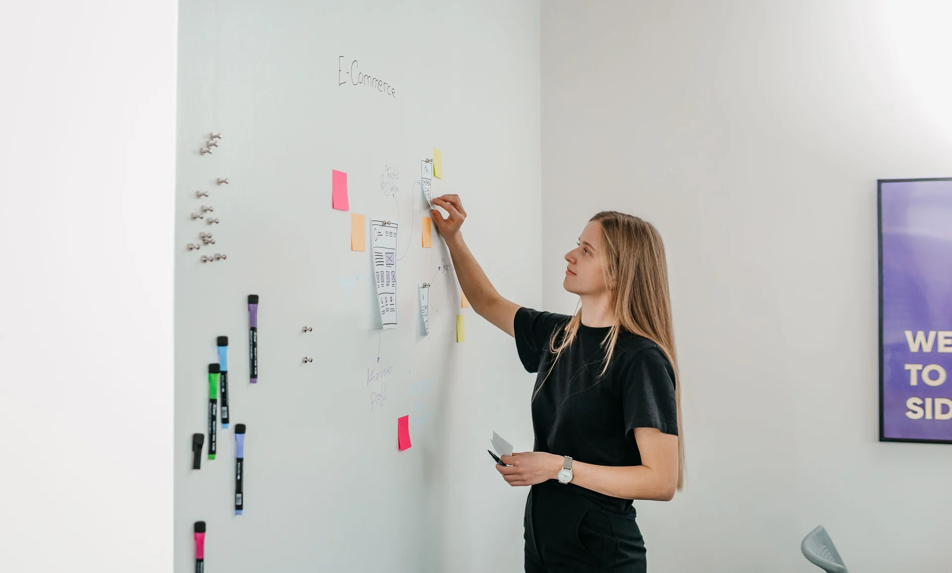 Junge Frau klebt bunte PostIts an ein Whiteboard