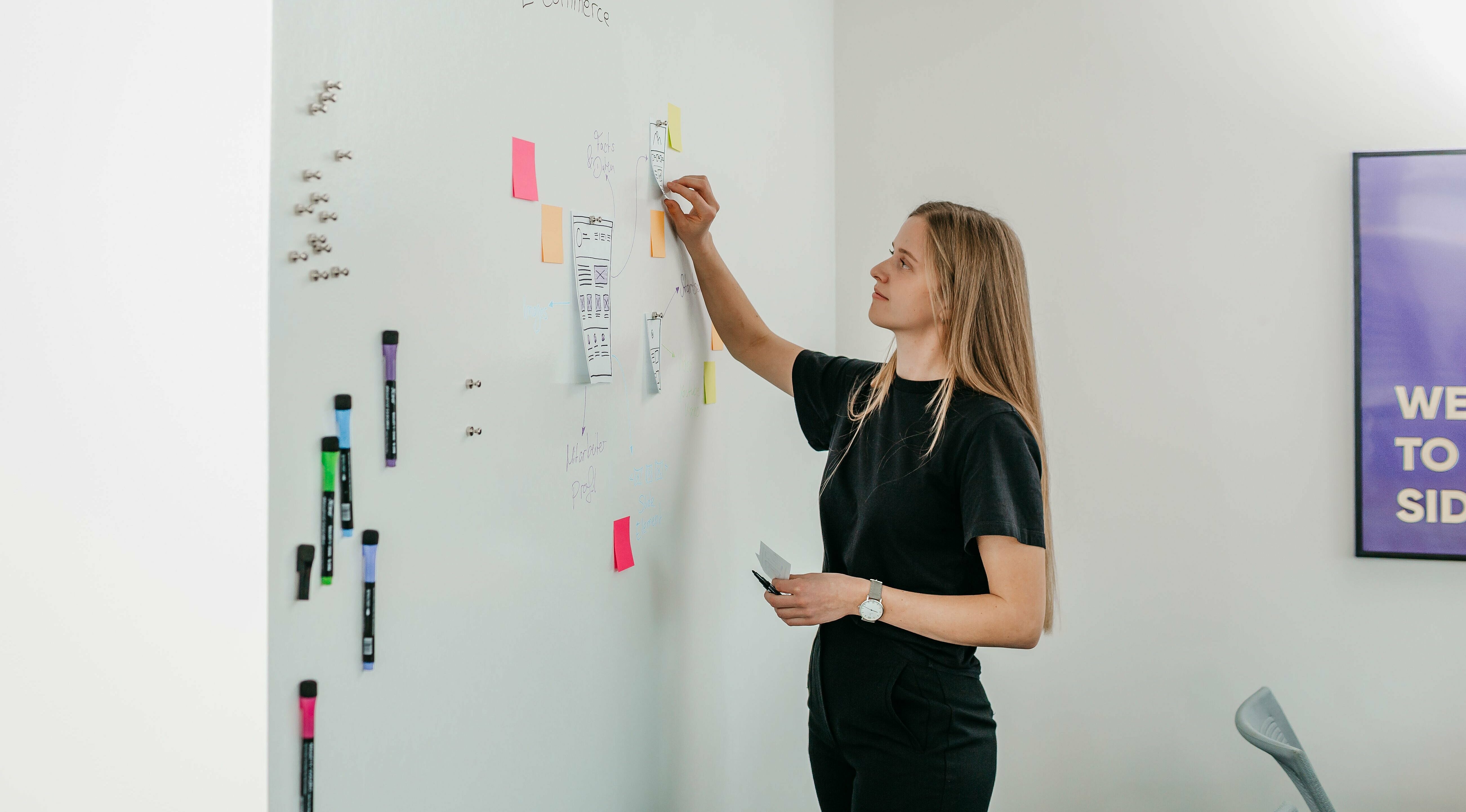 Junge Frau klebt bunte PostIts an ein Whiteboard