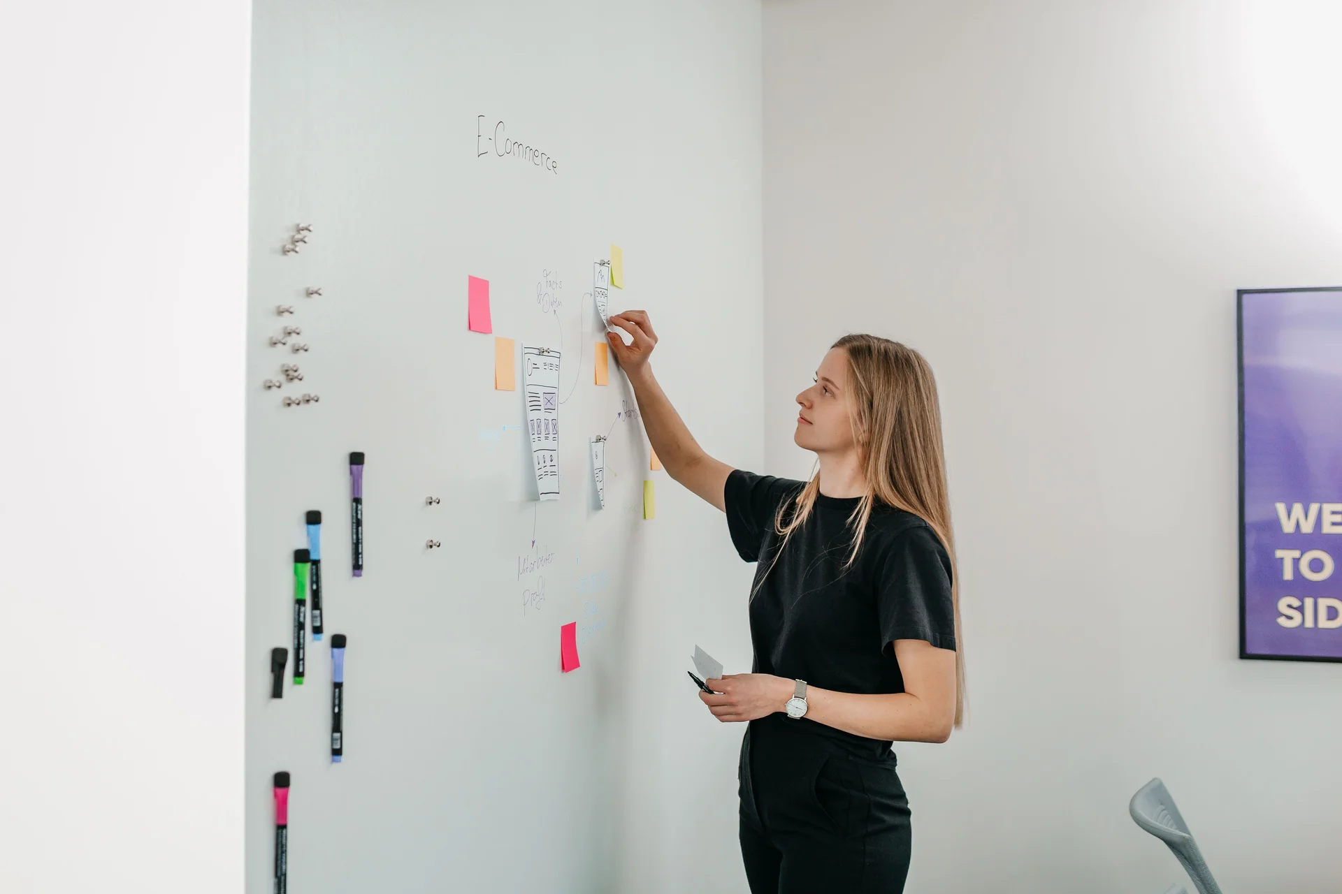Junge Frau klebt bunte PostIts an ein Whiteboard