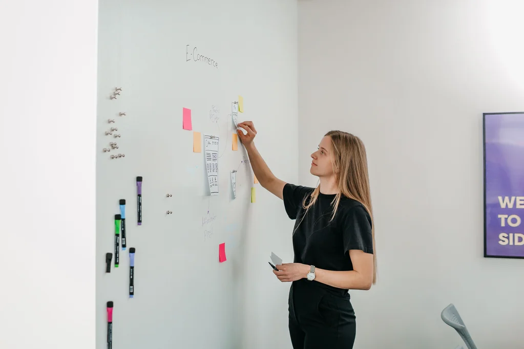 Junge Frau klebt bunte PostIts an ein Whiteboard