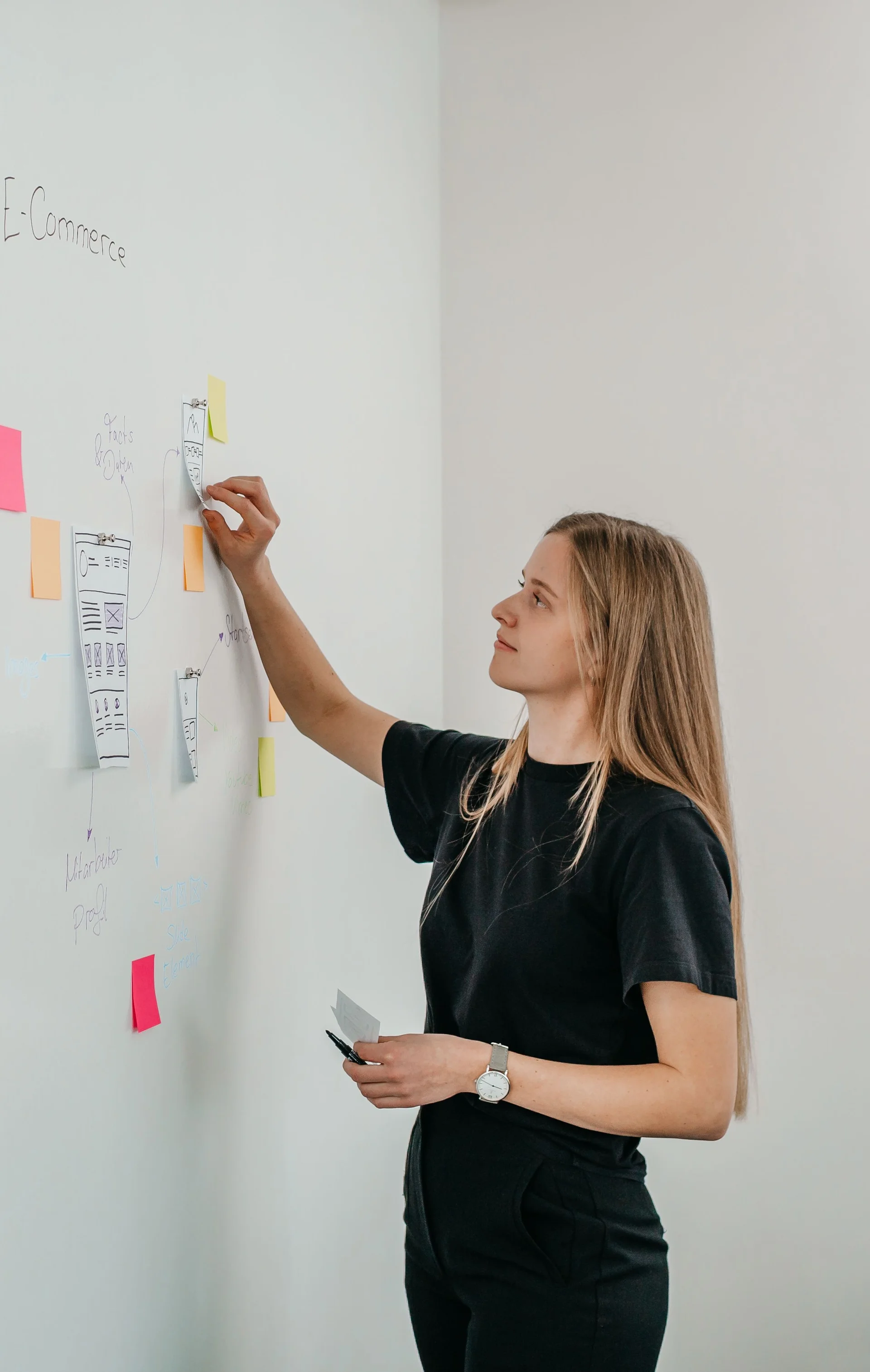 Junge Frau klebt bunte PostIts an ein Whiteboard