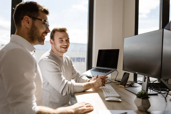 Zwei LightsOn Mitarbeiter stehen am Schreibtisch und schauen in den Monitor