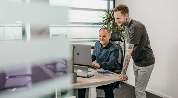 Zwei Mitarbeiter schauen zusammen in einen Laptop auf dem Schreibtisch