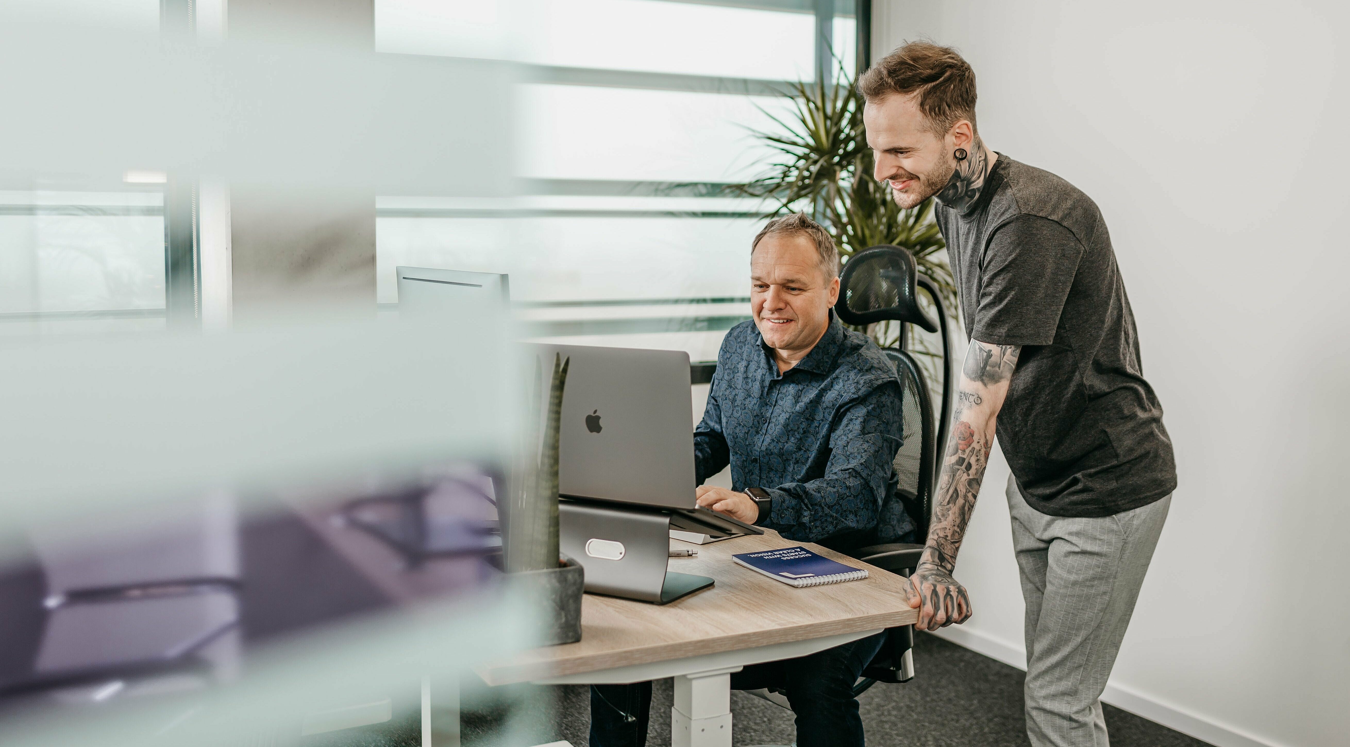 Zwei Mitarbeiter schauen zusammen in einen Laptop auf dem Schreibtisch