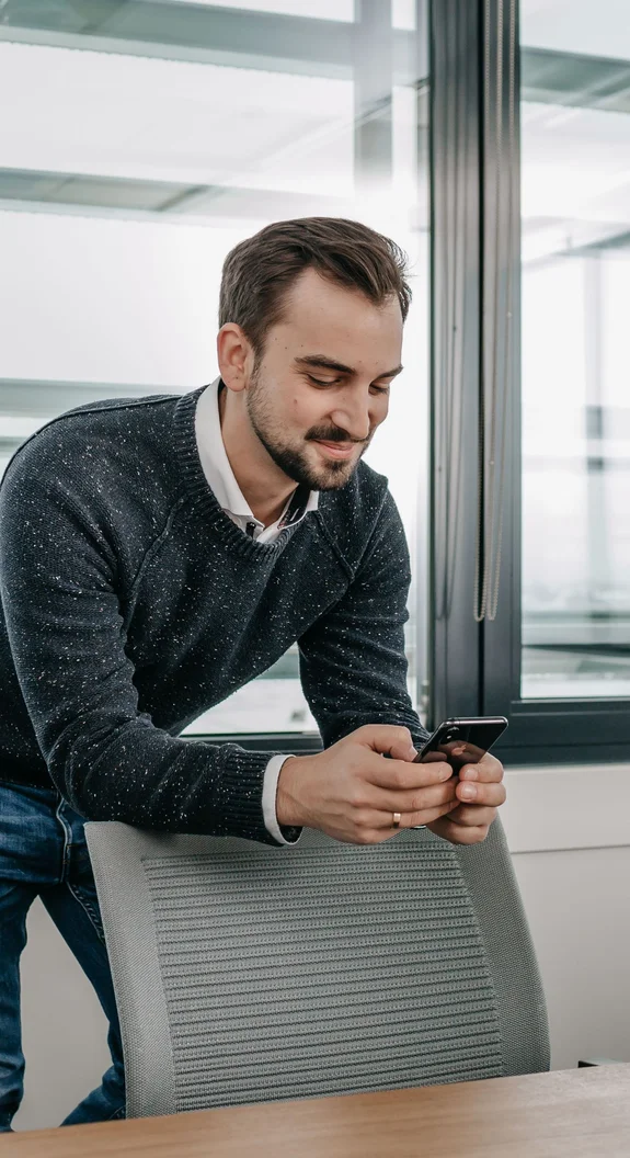 Mitarbeiter der Agentur LightsOn lehnt auf einem Stuhl mit Handy in der Hand