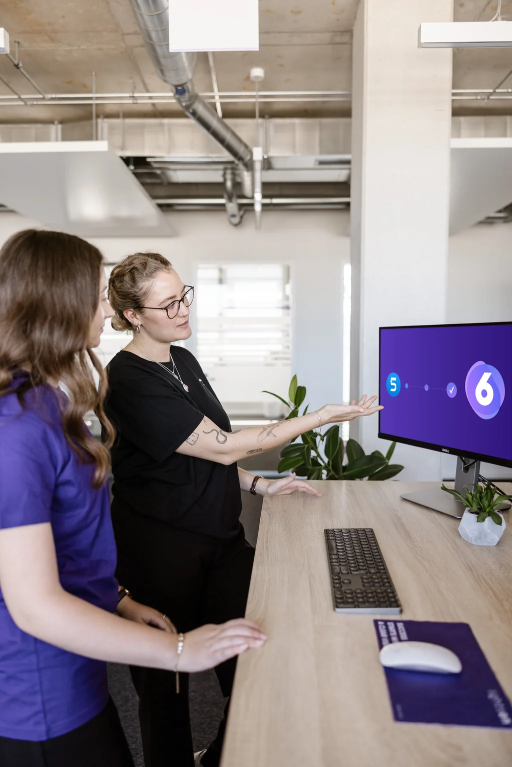 Zwei LightsOn Mitarbeiterinnen stehen am Schreibtisch und schauen in den Monitor