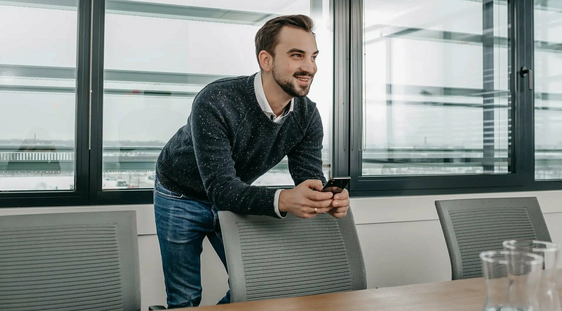 Mann lehnt mit Handy in der Hand auf einem Stuhl 